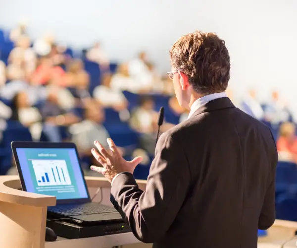A speaker with a laptop facing an audience